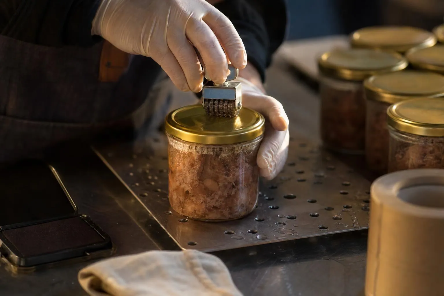 Main gantee inscrivant un numero au tampon dateur sur le couvercle metallique d un bocal pose sur une plaque de sterilisation